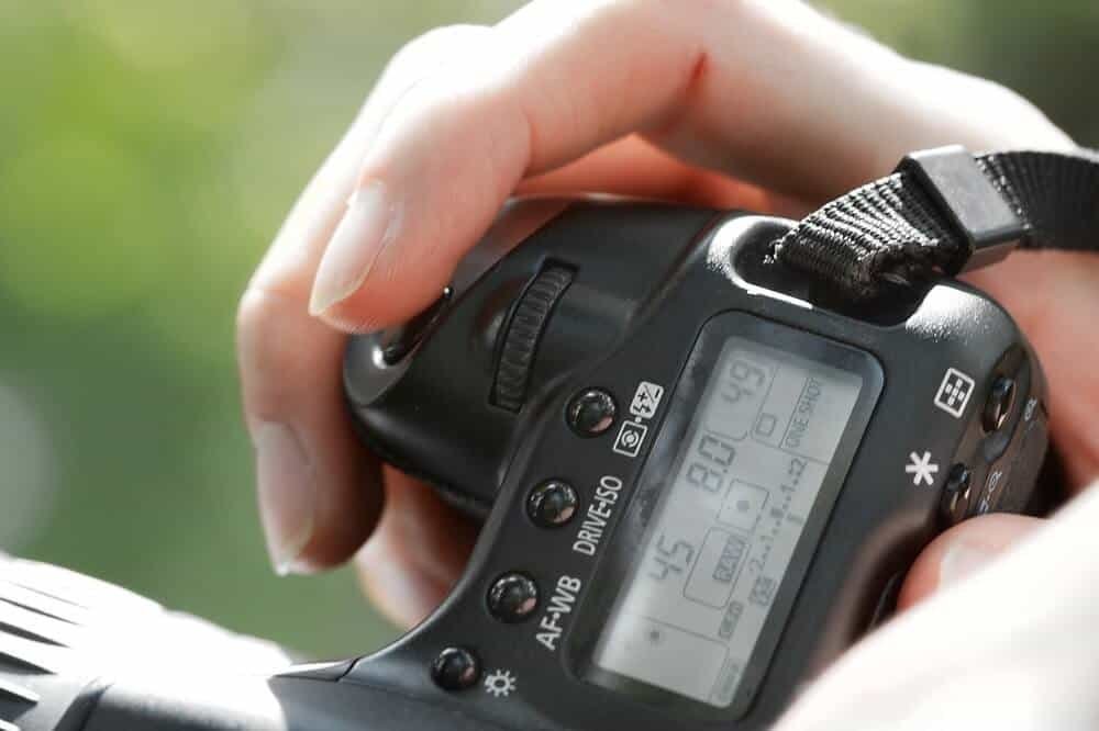 Man photographing outside on a sunny day looking at ISO settings in the DSLR camera screen