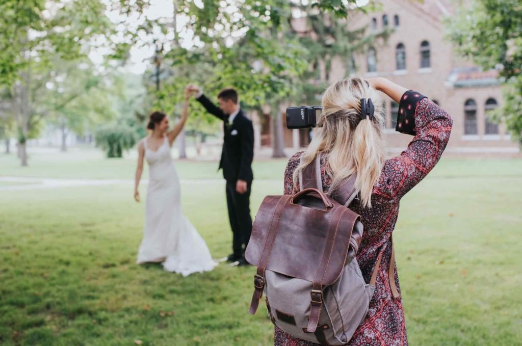 woman taking flash photos of wedding couple outdoors.