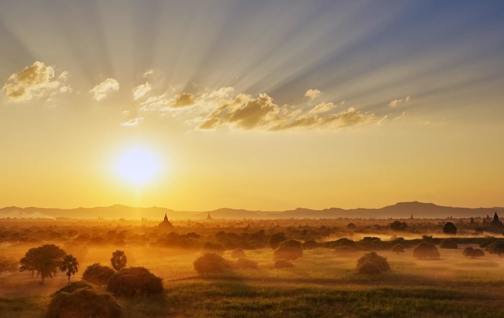 wide landscape photo of fields and mountains against a sunrise.