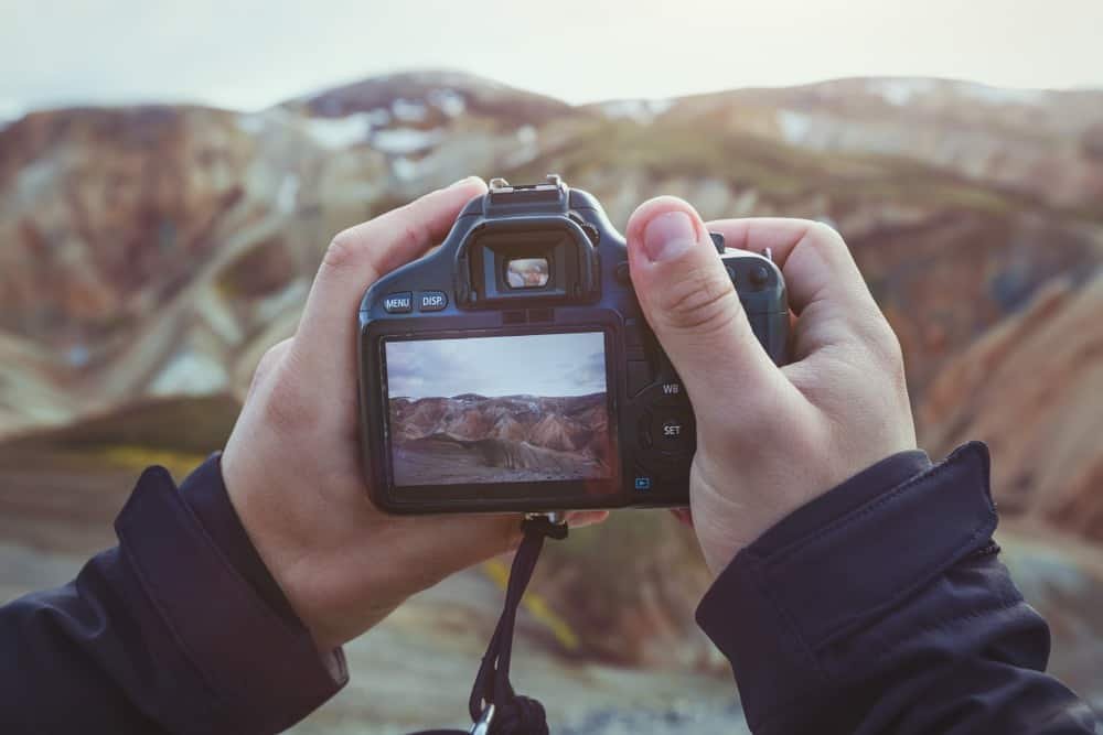 Landscape travel photographer hands holding camera and taking photo of mountains