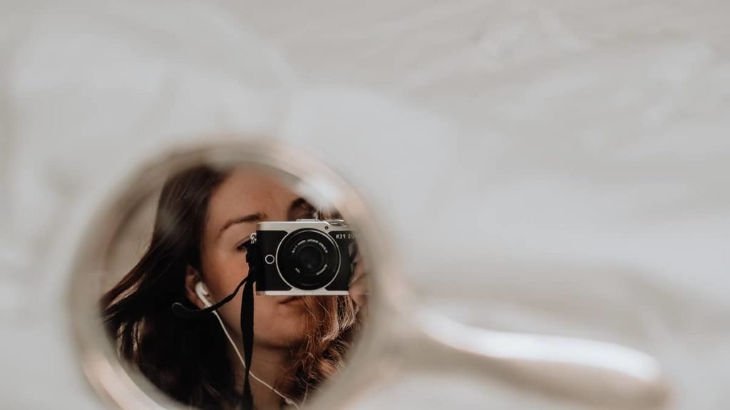 girl taking self-portrait in small mirror using mirrorless camera