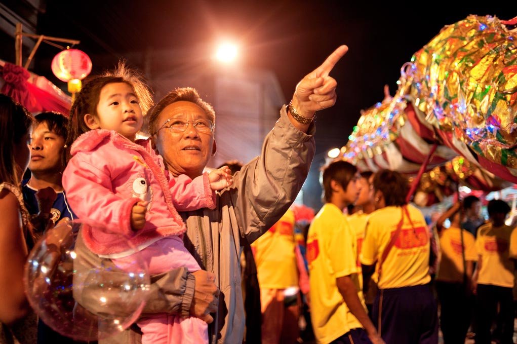 man holding a child as he points to something during an evening festival.