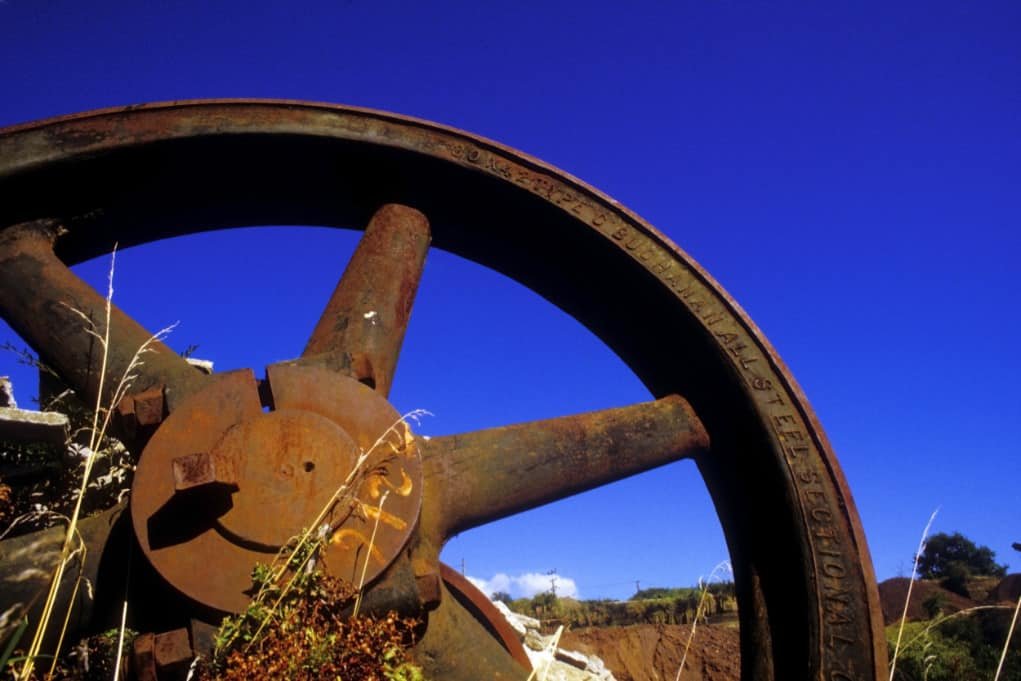 Large rusty iron wheel against blue sky.