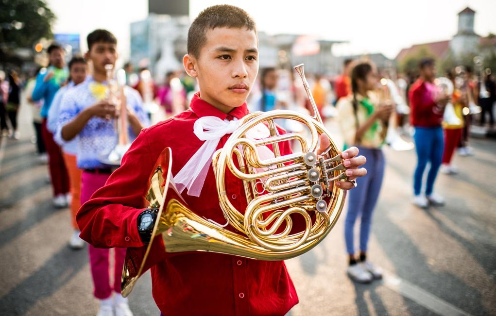 A young man plays a French horn during during a parade