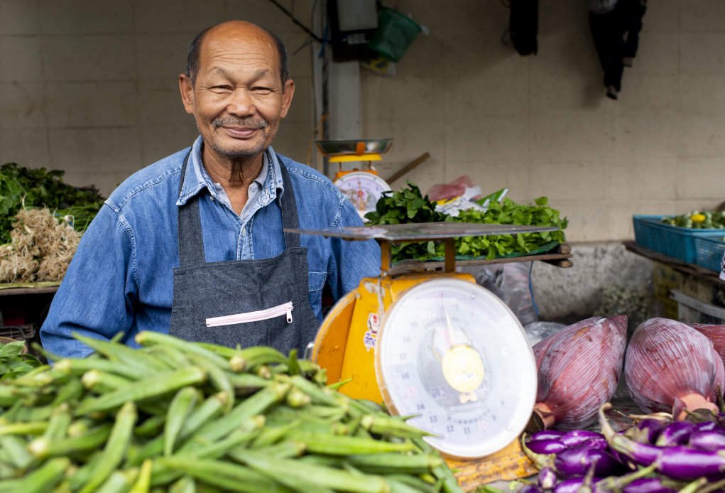 environmental portrait of a market vendor selling vegetables.