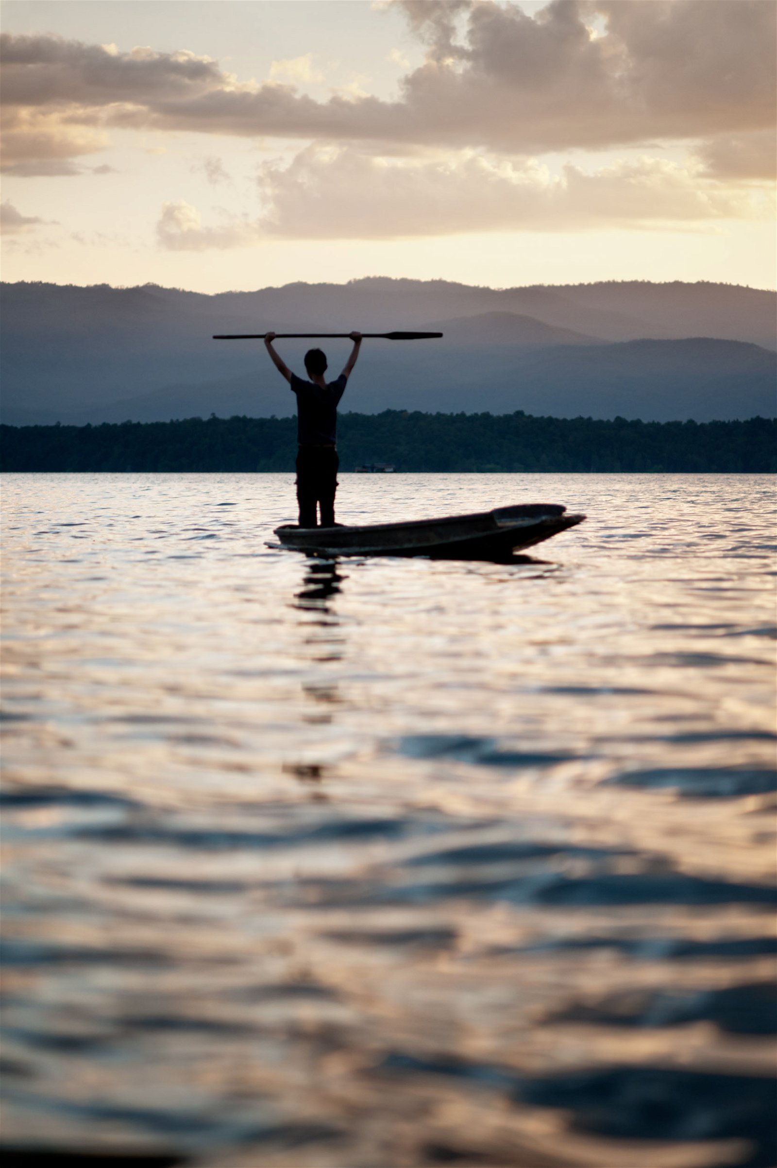 example image of a man paddles a traditional canoe on a lake at sunset.