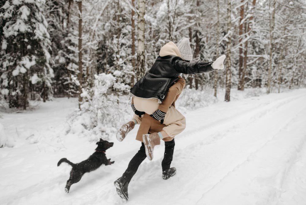 Couple run through snow forest on a shoot.