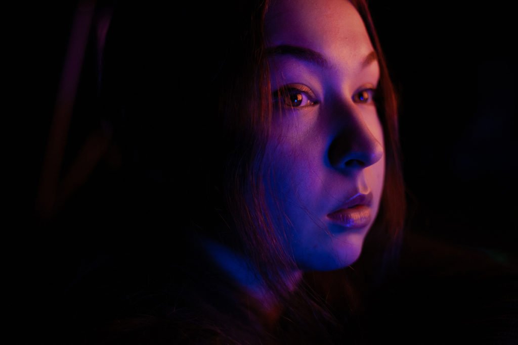 Portrait of a girl looking into the distance. Her face is lit by blue and red artificial lights.