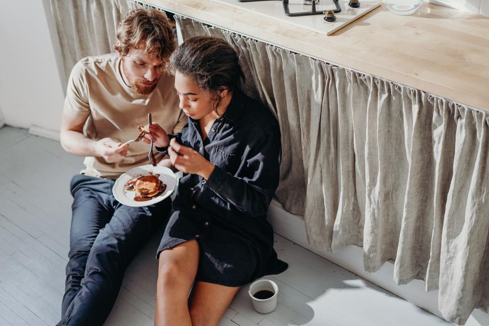 Couple share breakfast together at home on the floor.
