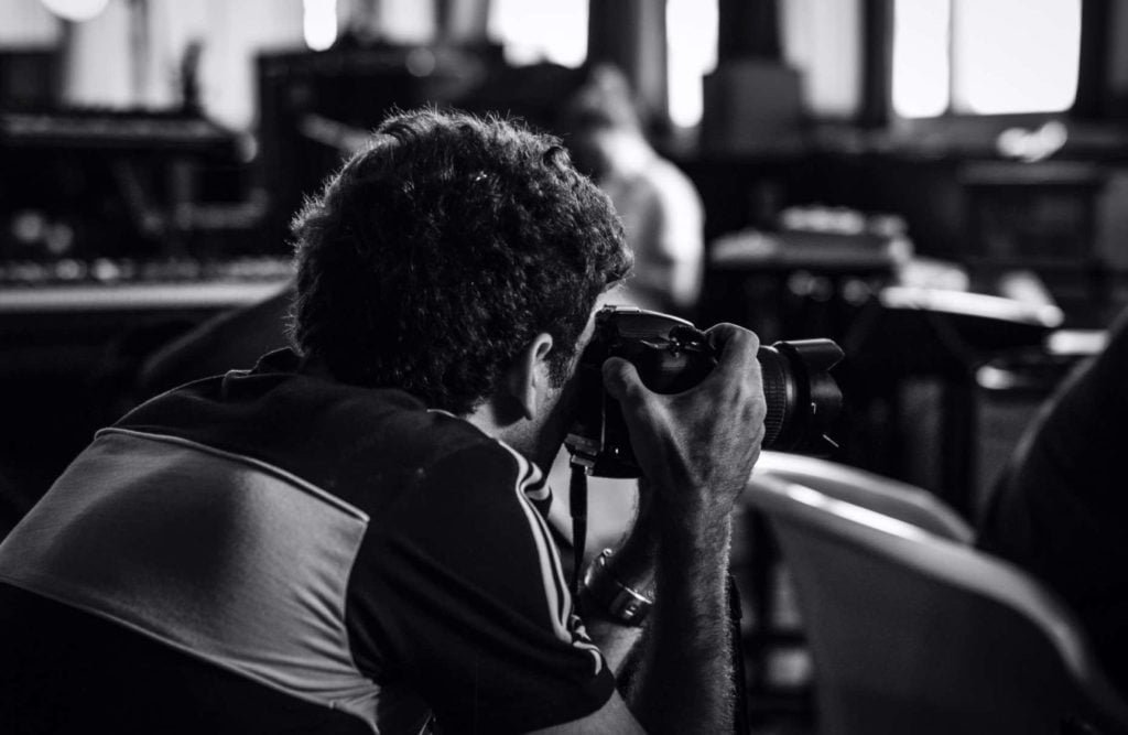 black and white portrait of man taking photographs in an indoor space.
