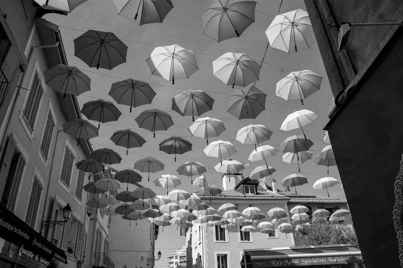 black and white street photo of umbrellas hanging in the sky.
