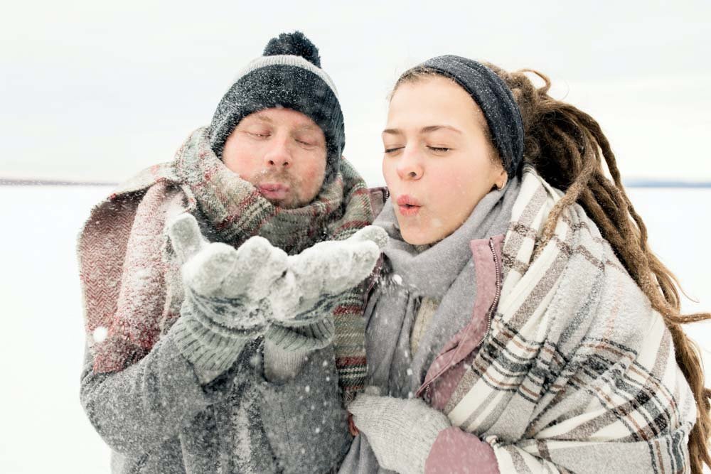 Couple blowing snowflakes towards camera.