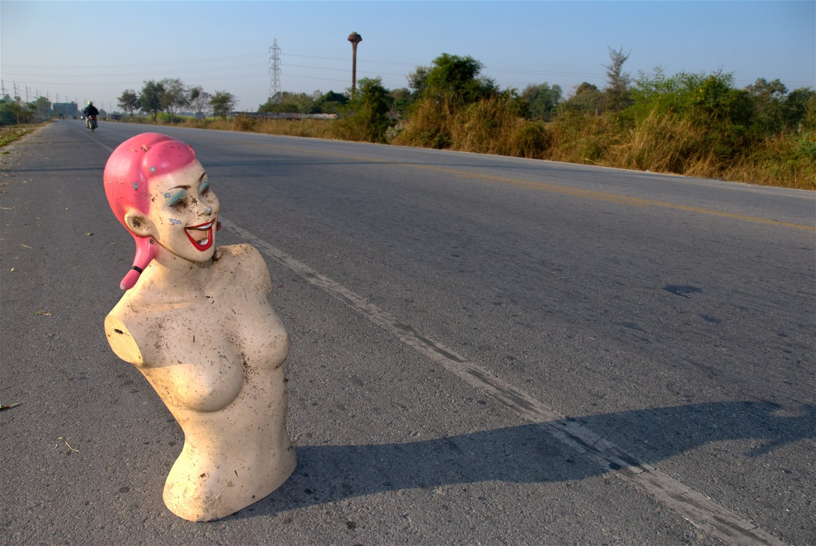 Mannequin on the space at the side of an empty road.