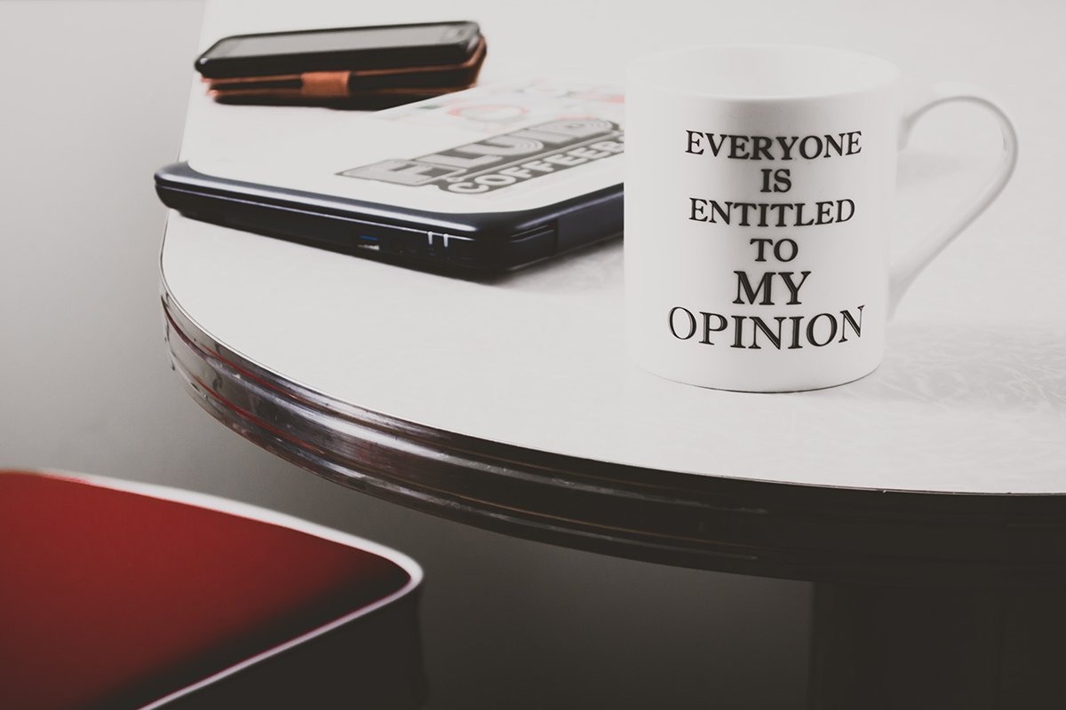 minimalistic shot of laptop, phone, and mug with the words 'everyone is entitled to my opinion' written on it.