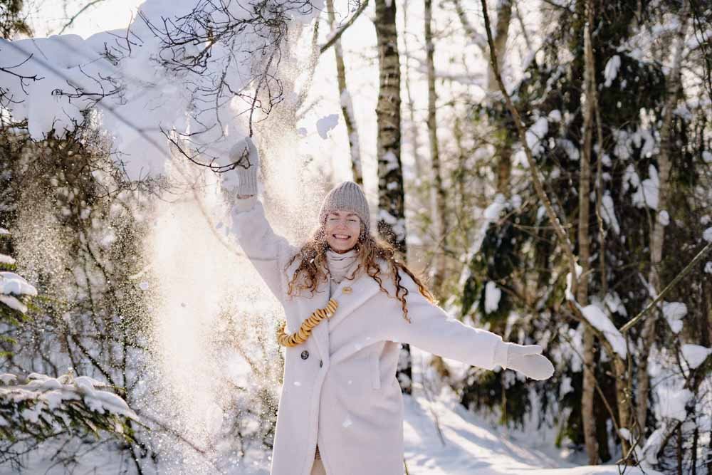 Woman in coat dances in snow with sunshine at the back.