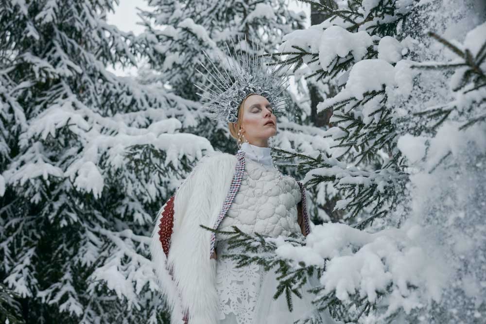 woman stands in snow filled scene for winte photoshoot.
