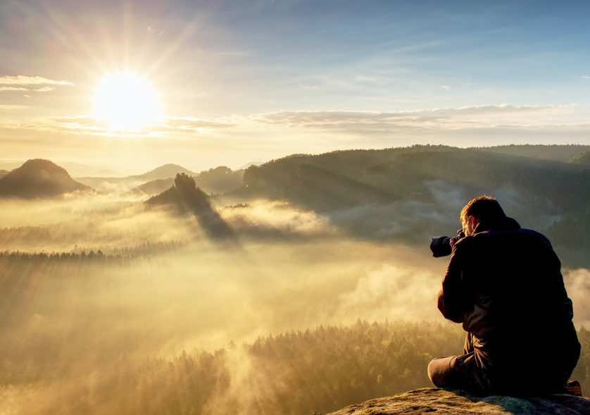 man taking photos of sunrise over a mountain