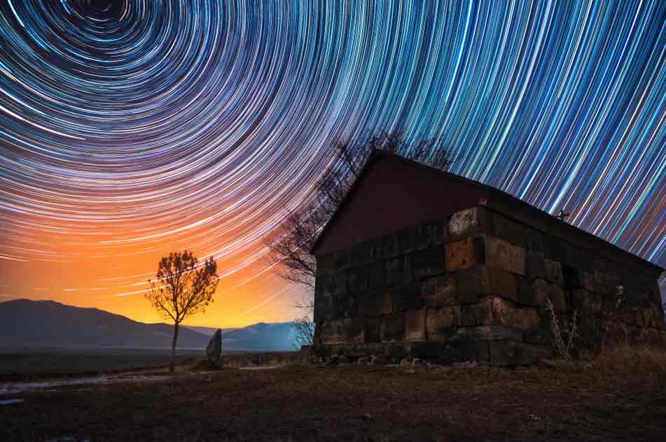 light trails in a dark night sky over an old farm building.