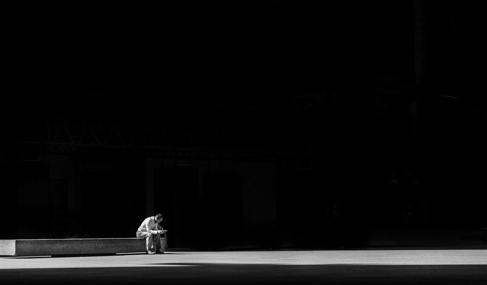 minimalistic black and white image of man sitting on a bench in a dark space.