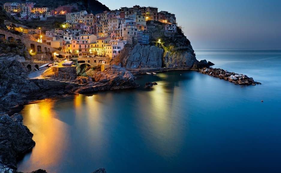 night landscape of Cinque Terre Italy with light reflecting on the night lit water.