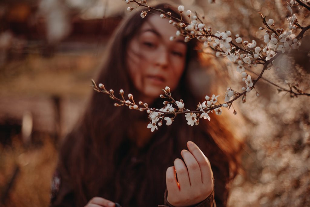 Creative out-of-focus portrait of a girl posing behind a cherry blossom branch.