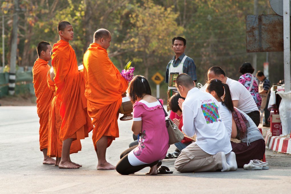 people and monks gathered on a street in Thailand