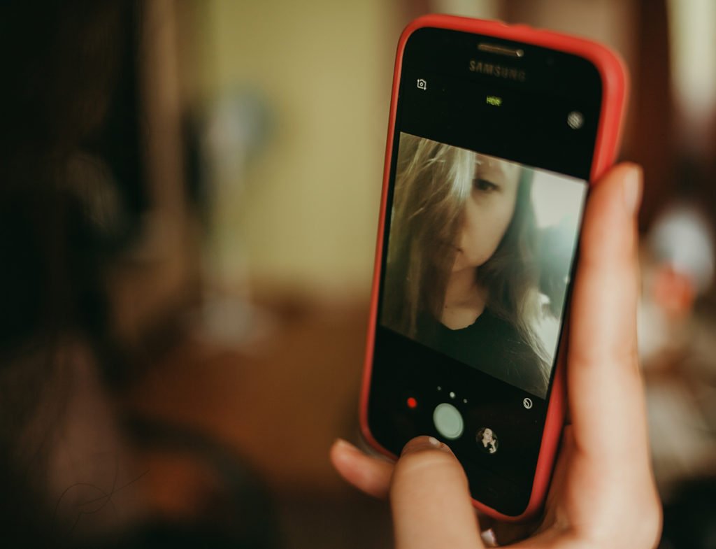 Model with a smartphone camera in selfie mode, using shallow depth of field.