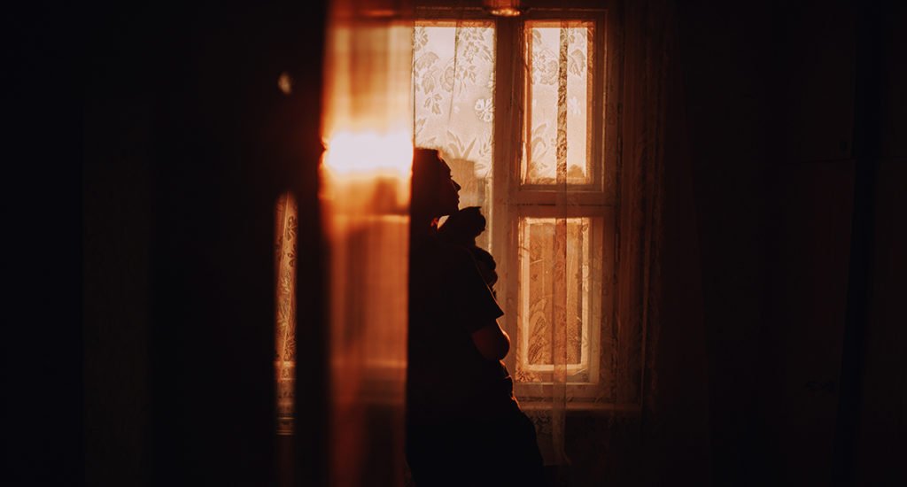 Cinematic self-portrait of a silhouette. Looking out of the window while holding her cat.