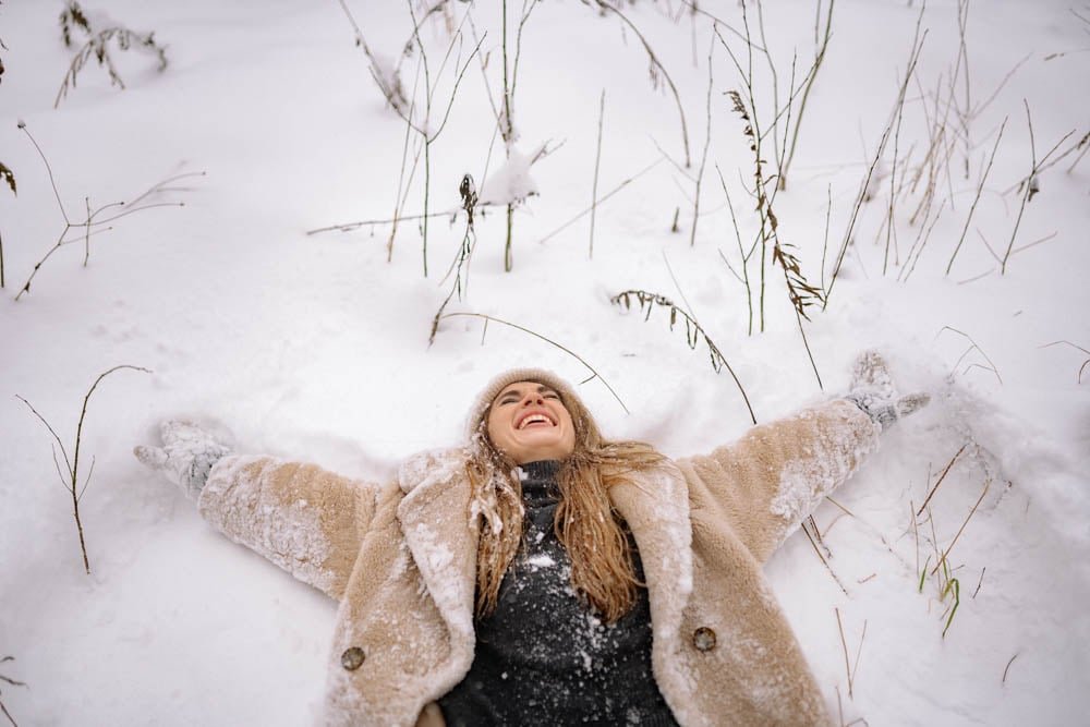 Woman laying on ground in snow for fun portrait.