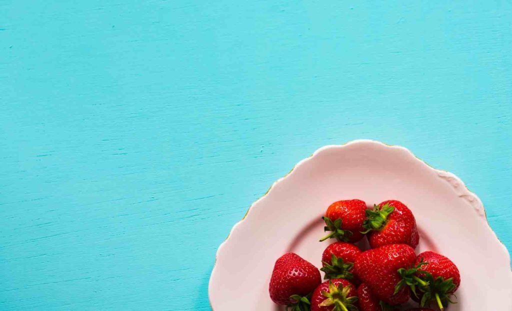 strawberries on white plate with blue background.