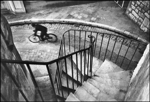 Man on bike riding past stairs. Cartier bresson street in black and white.
