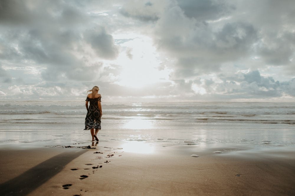 woman walks towards cloudy sunset on the beach.