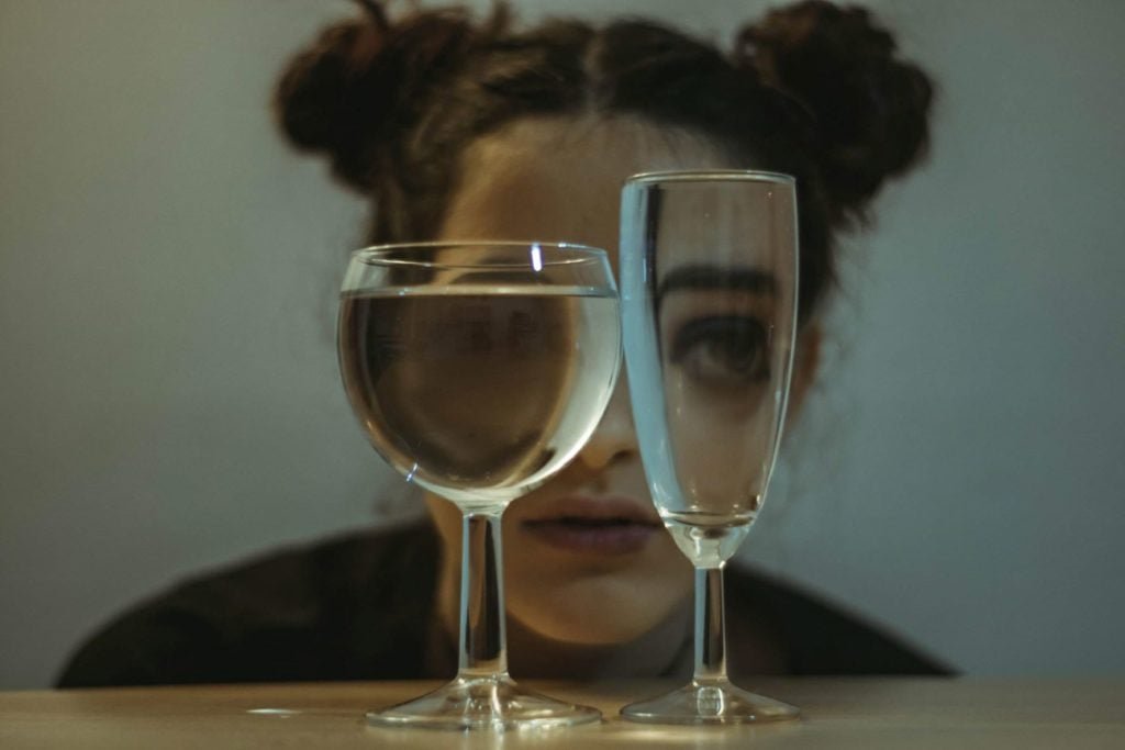 close up of woman looking through two different shapes of glasses one full one empty.