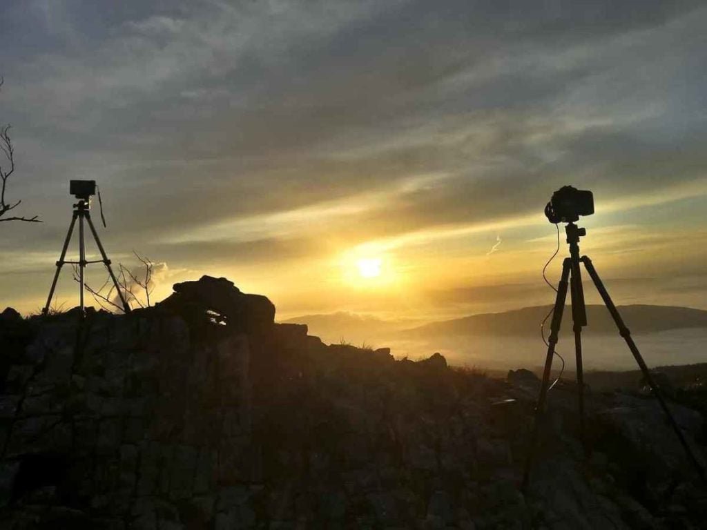 two cameras on tripods with sunrise in the background.