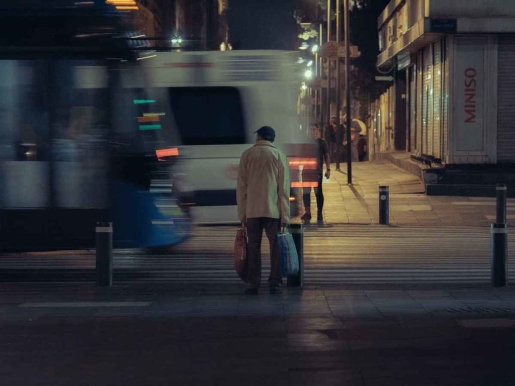 man holding bags waiting to cross the street vehicles motion blur.
