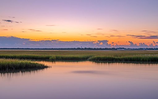 sunrise photo of tidal marsh, water, and clouds.